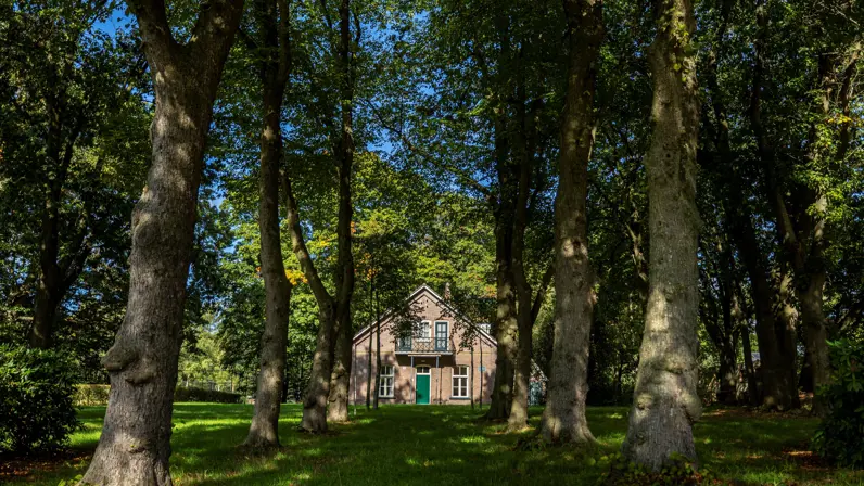  Een kazernewoning met ervoor een laan met bomen.  