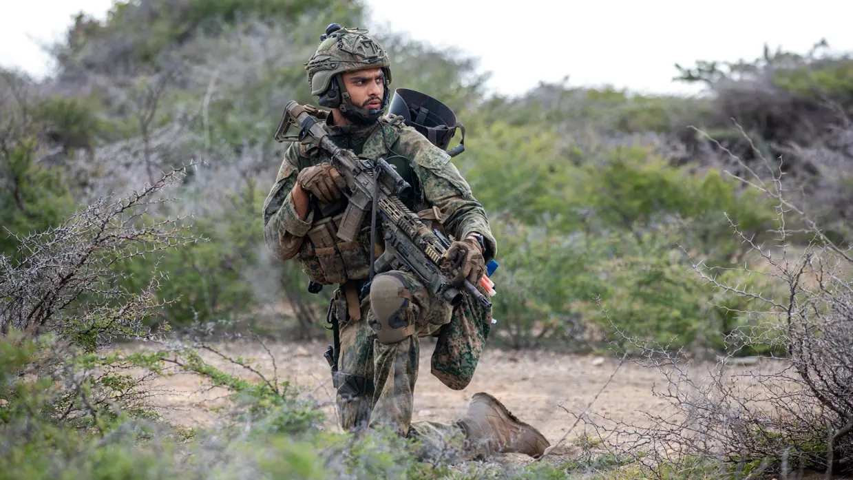 Een militair zit op een knie en tuurt in de verte. 