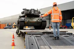 Militair voertuig wordt op een wagon gereden.