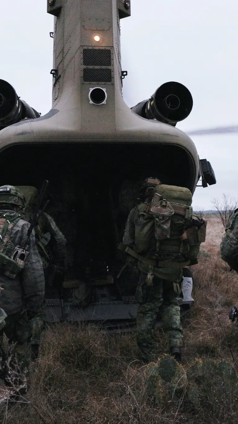 Militairen in het veld lopen via de laadklep een Chinook met draaiende rotors in.