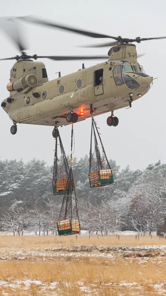 Een helikopter maakt een landing op een wit veld. Rechts met een paar pakketten onder zich. 