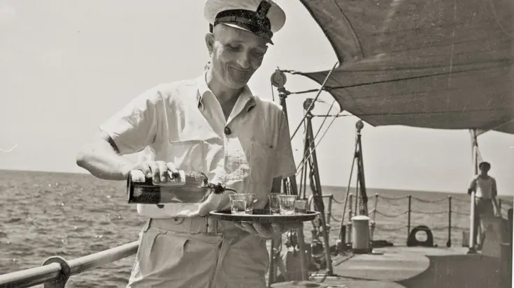  Een hofmeester serveert drankjes op het dek van een marineschip in 1948.
