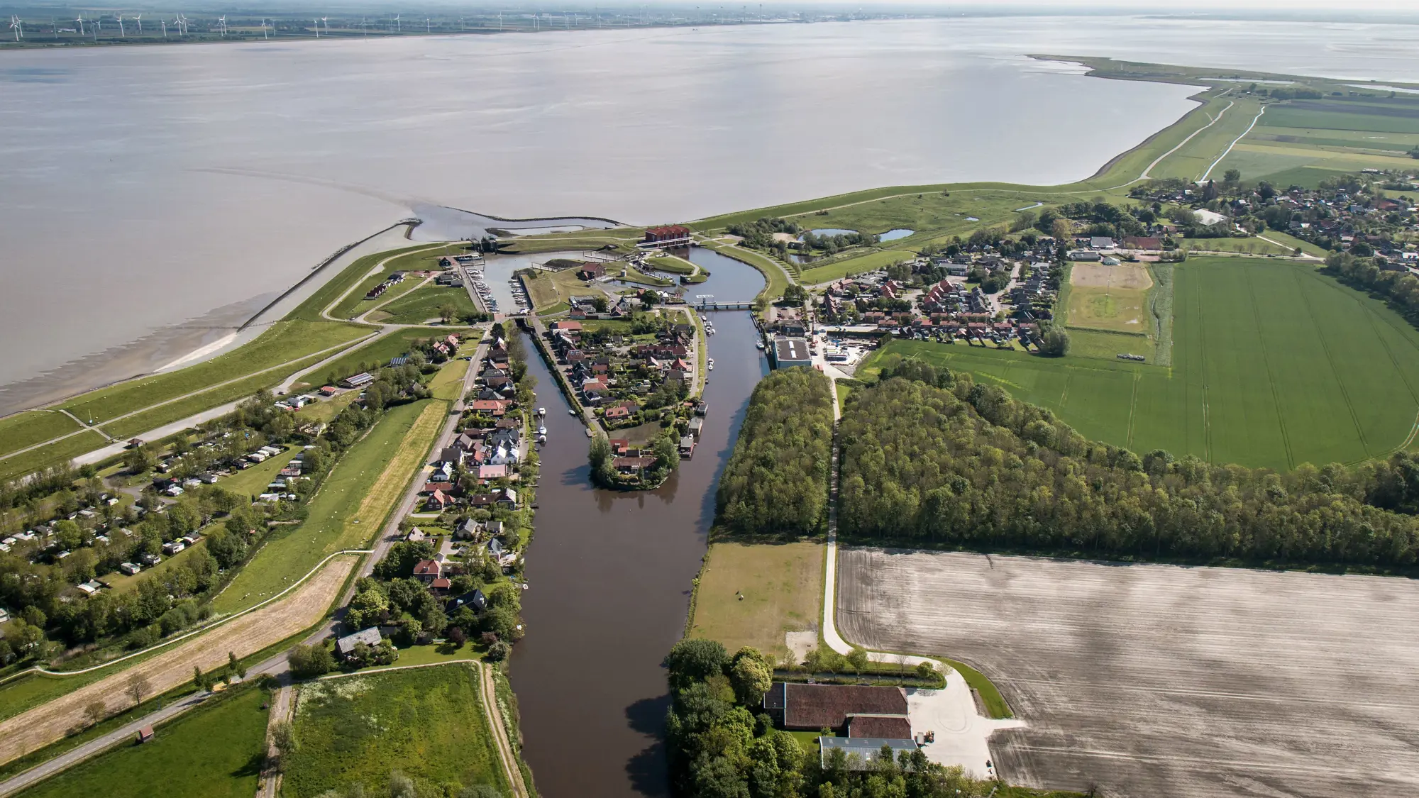 Luchtfoto van grensgebied tussen land en zee, met huizen en haven.