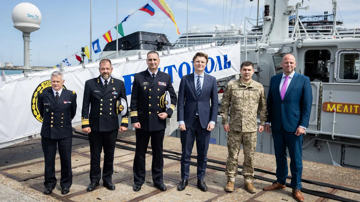 Militairen en bewindslieden poseren voor een schip.