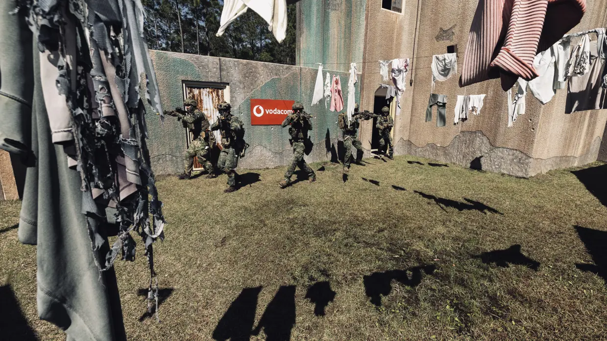 Mariniers lopen langs wasgoed dat in een tuin van een oefenhuis is opgehangen.  