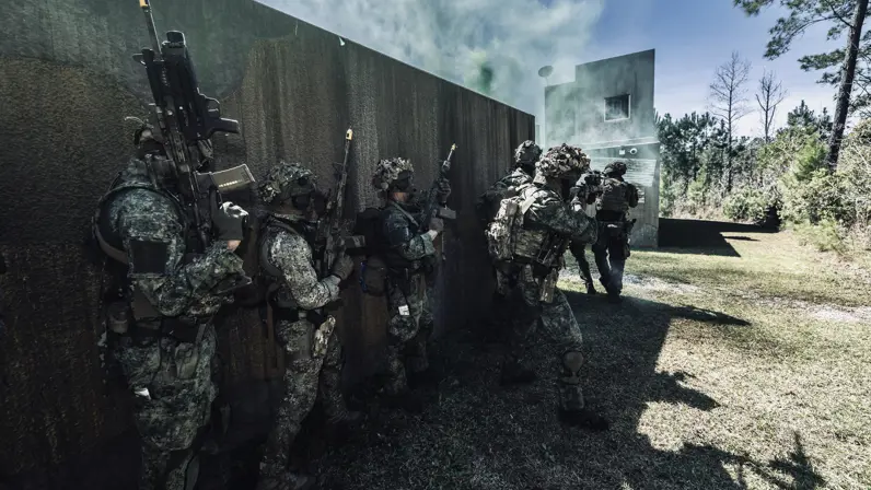 Een groep mariniers staat met wapens in de aanslag achter een muurtje, terwijl de voorste het vuur openen.    