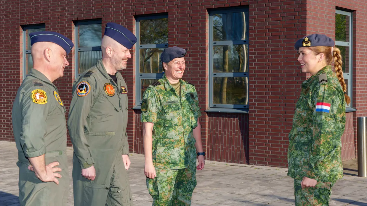 Luitenant-generaal André Steur, generaal-majoor Robert Adang en kolonel Martine Verhulst staan tegenover prinses Amalia buiten voor de Luchtmachttoren. Ze lachen naar elkaar en dragen allen operationele uniformen.