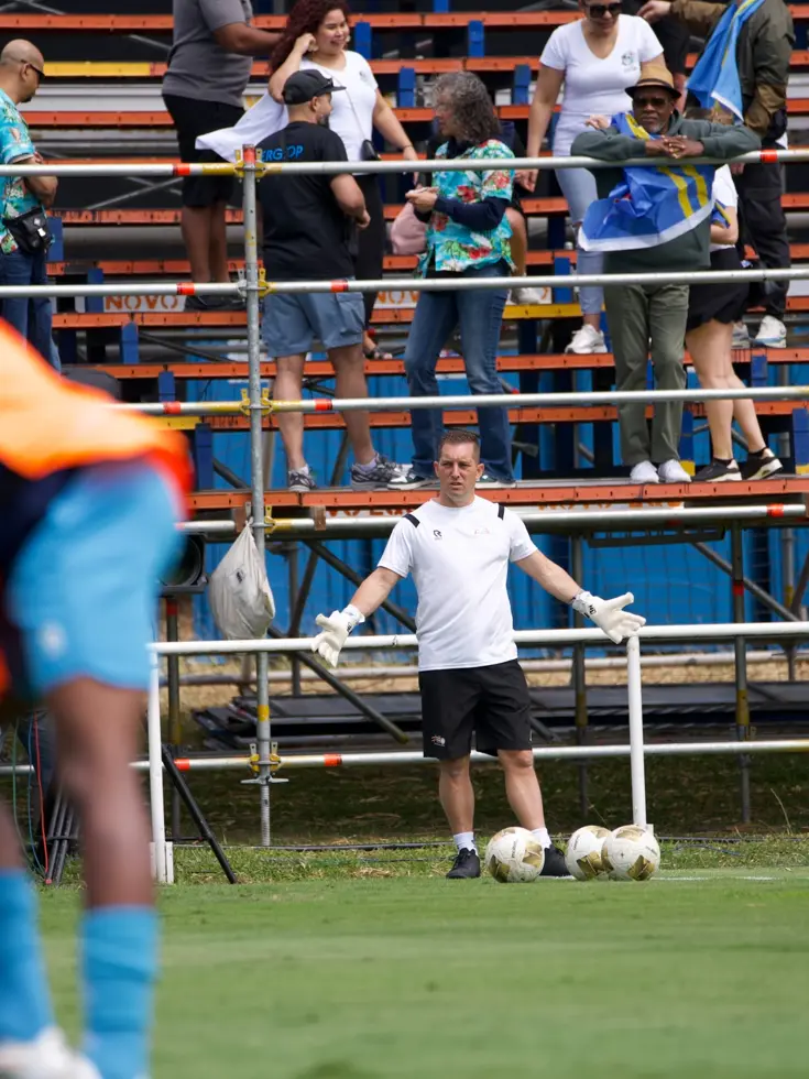 Een keeperstrainer staat op trainingsveld met gespreide armen achter een viertal ballen. 