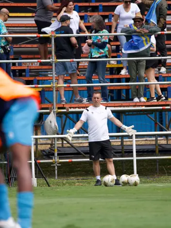 Een keeperstrainer staat op trainingsveld met gespreide armen achter een viertal ballen. 