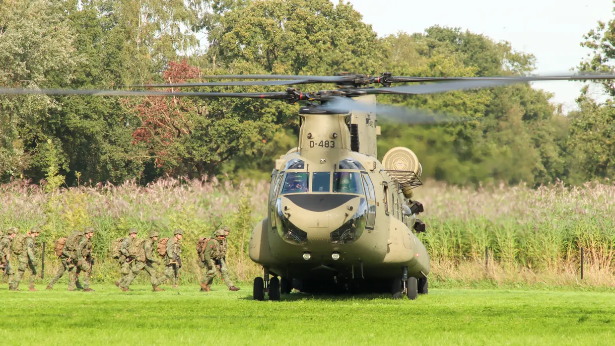 Gehelmde soldaten lopen door het gras naar een grote helikopter.