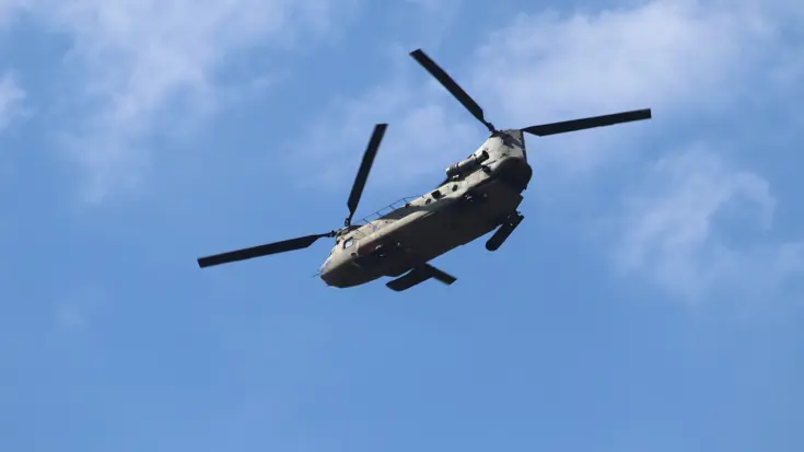  Een grote militaire helikopter vliegt door de blauwe lucht. De rotorbladen lijken stil te staan.