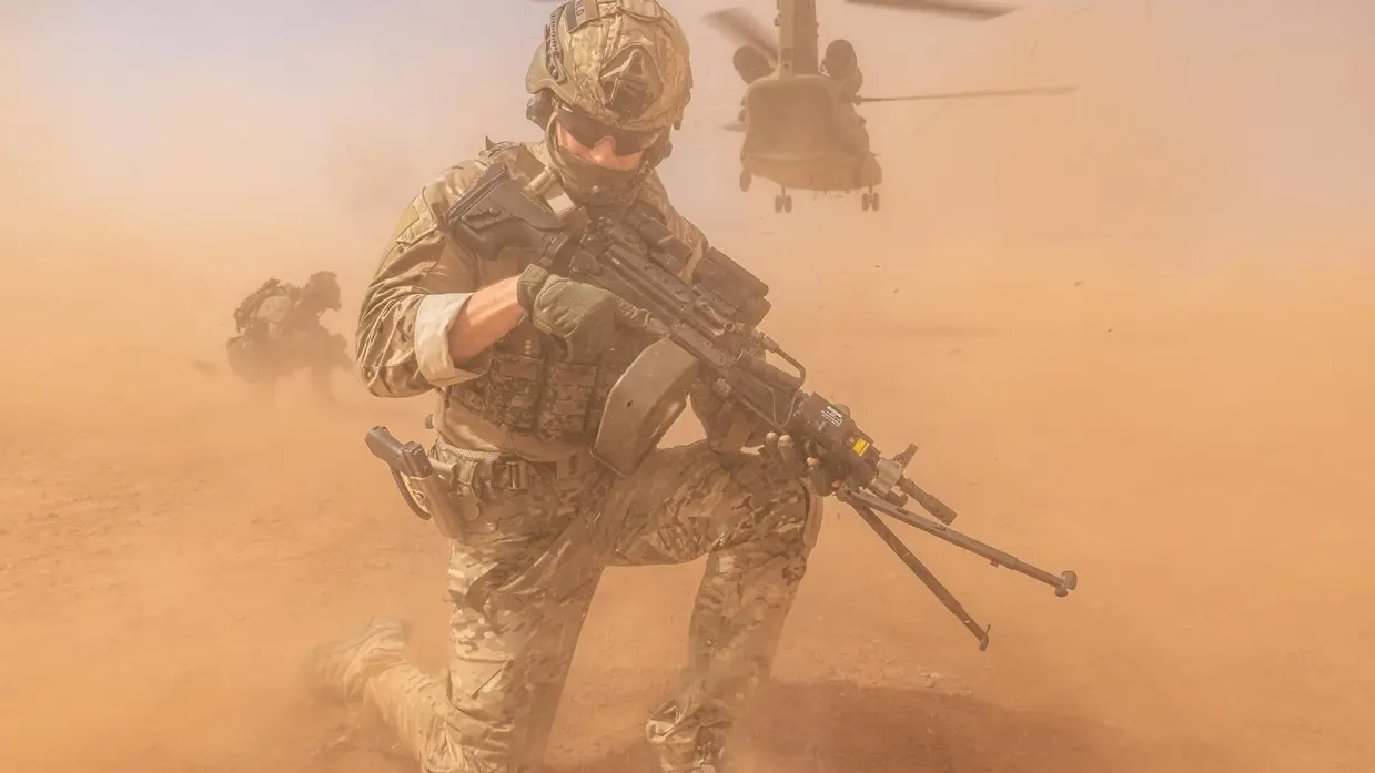 Een militair met op de achtergrond een opstijgende helikopter.