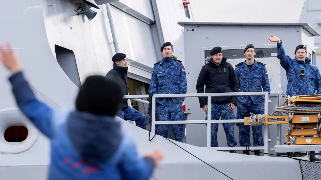 Militair aan boord van schip zwaait naar kind op kade. 