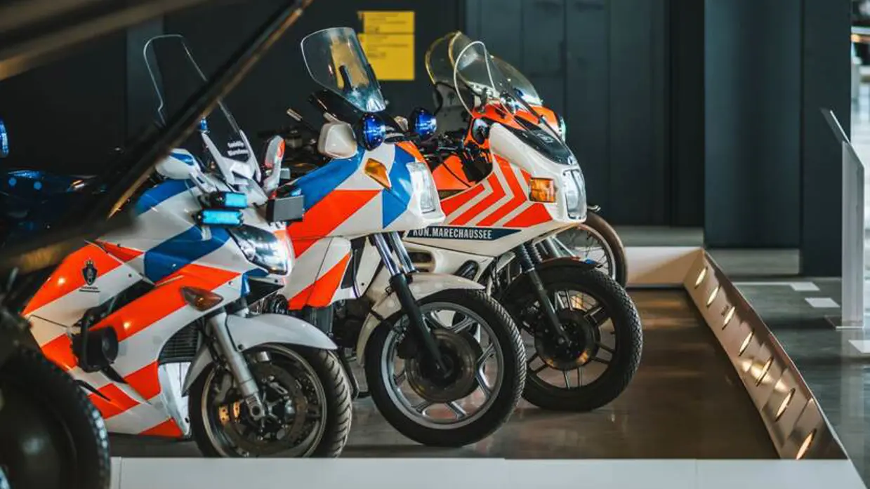 Rood-blauw gestreepte motoren van de marechaussee op de museumvloer.