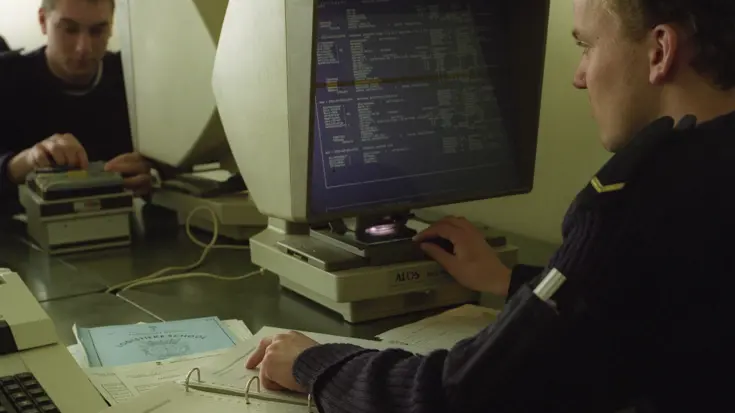 Een matroos zit achter een computerscherm en heeft een ordner voor zich liggen 