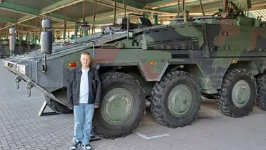 Een jongen poseert voor een groot groen pantservoertuig.