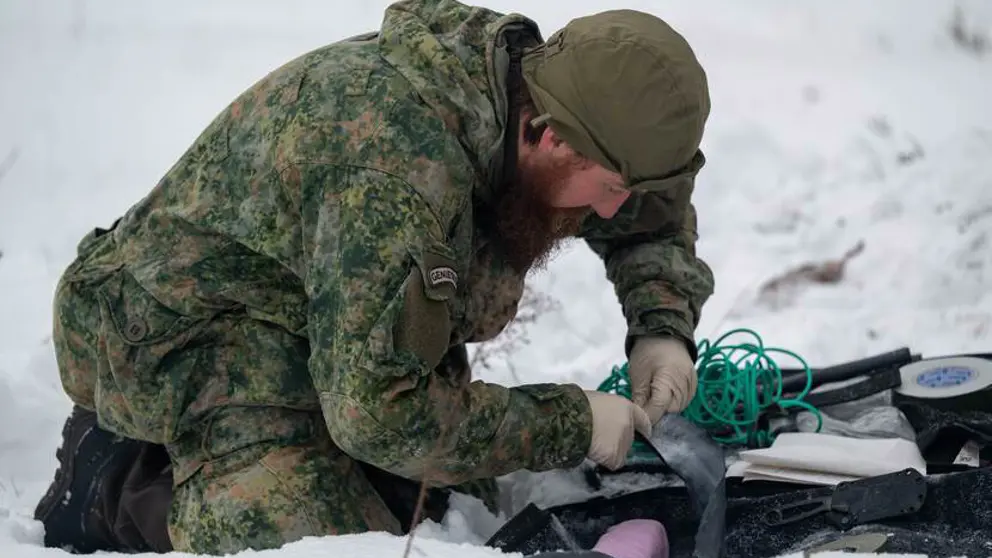 Militair op knieen in de sneeuw bezig met bevestiging van draden.