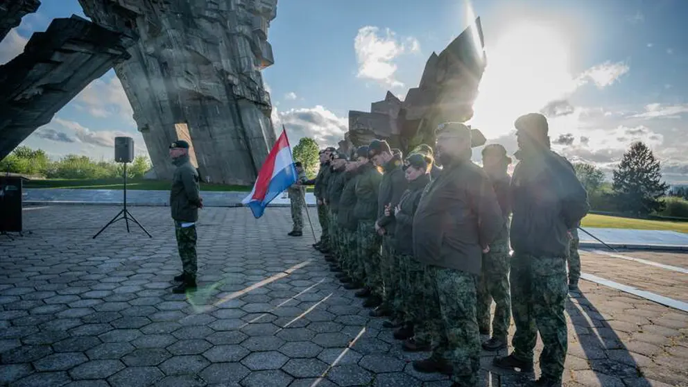 Militairen staan in de houding terwijl een van hen de Nederlandse vlag vasthoudt.