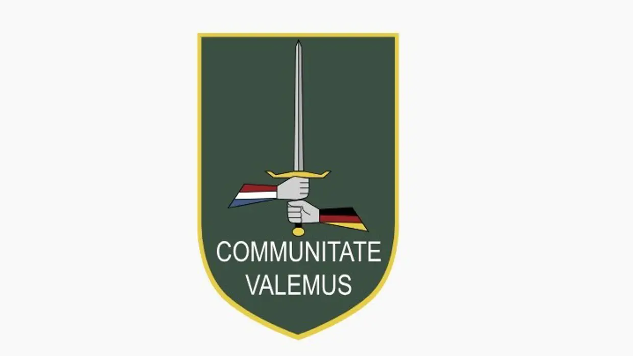Groen wapenschild met daarop een zwaard dat wordt vastgehouden door een 'Duitse' en een 'Nederlandse' hand. De spreuk ‘Communitate valemus’ betekent ‘samen zijn we sterk’.