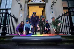 Defensiemedewerkers, onder wie de hoogste generaal, rollen een loper uit in regenboogkleuren.