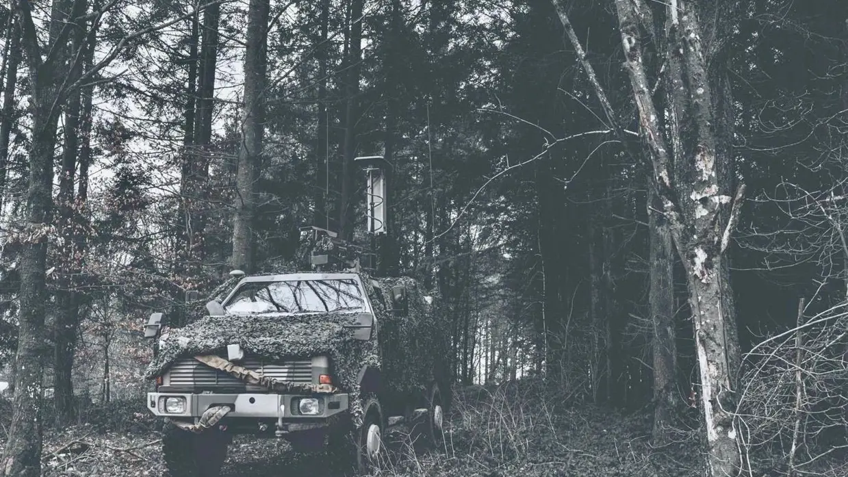 Jeep met camouflage net in het bos.