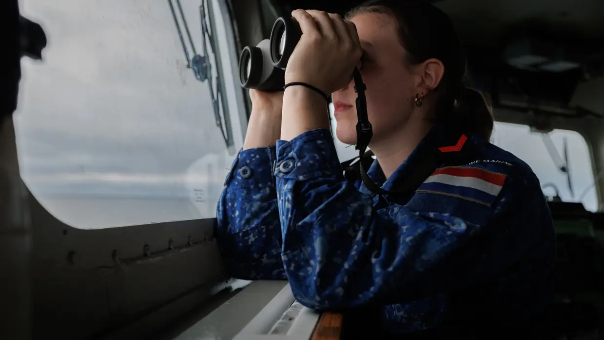 Een vrouwelijke marine-militair kijkt door een verrekijker.
