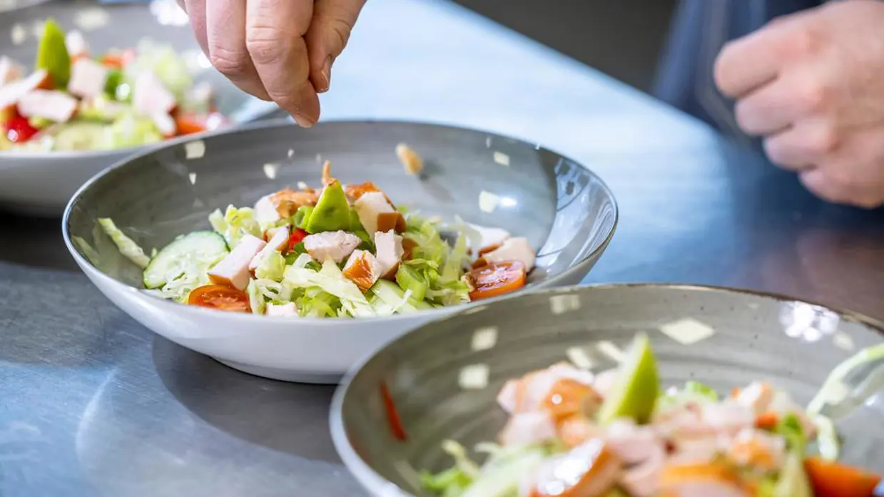 Een hand strooit iets over een bord met eten.