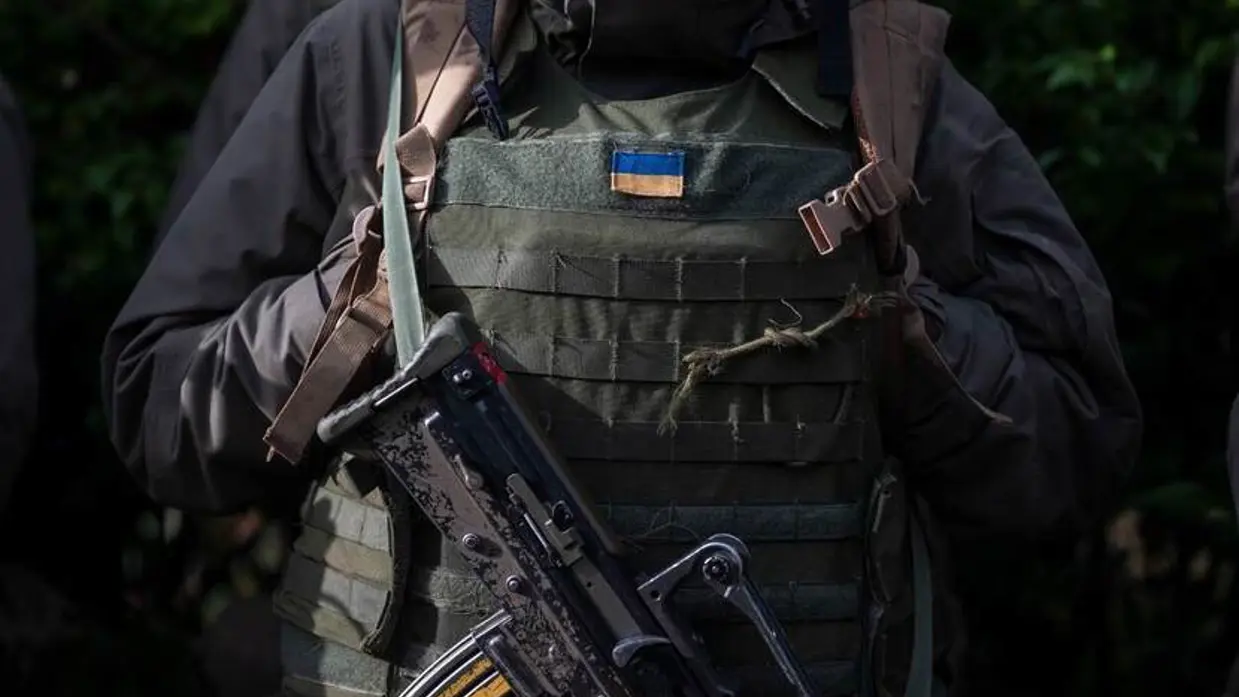 Vest van militair met Oekraïense vlag erop. Voor de borst hangt een machinegeweer.