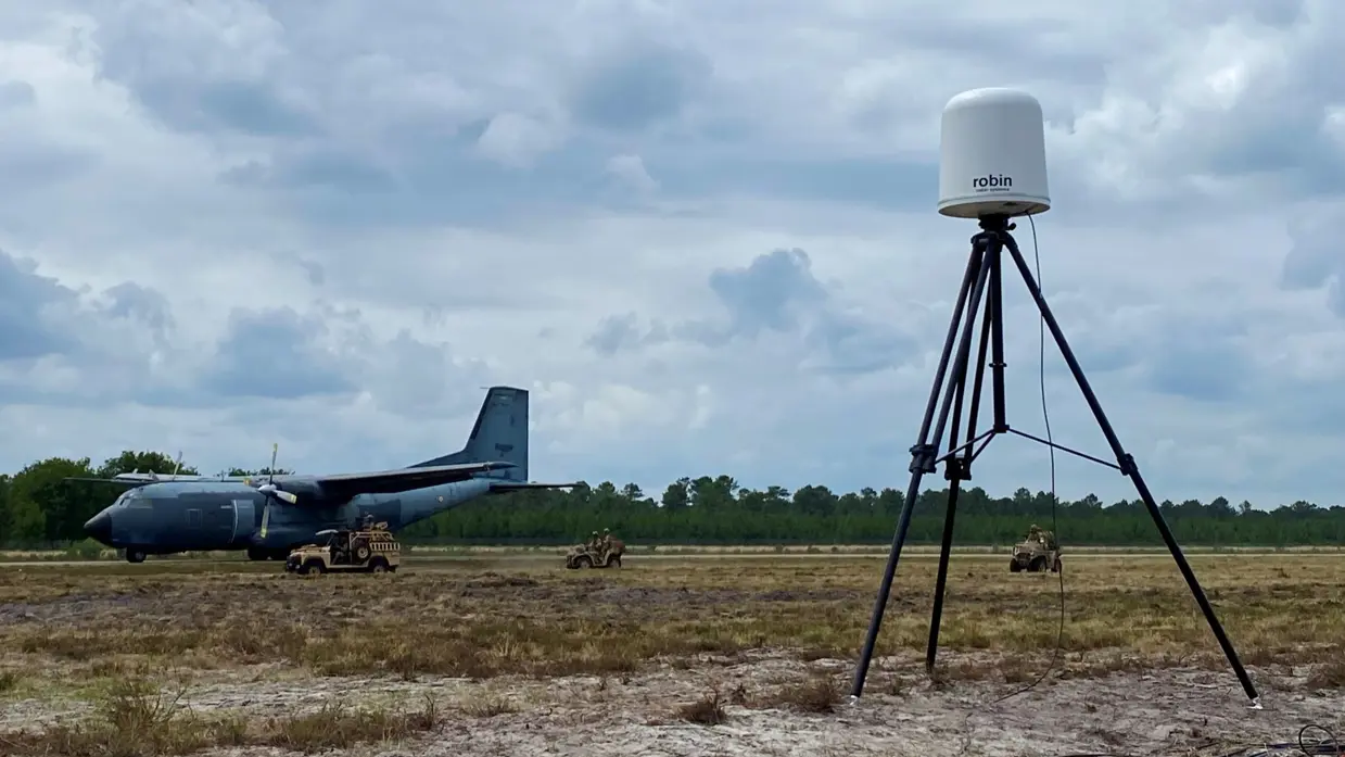  Een radarsysteem in een veld, daarachter een militair vliegtuig.