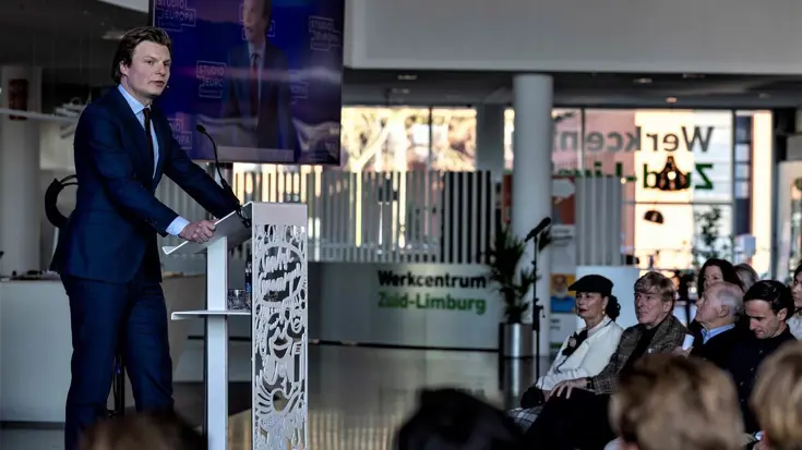Man achter spreekgestoelte spreekt zaal toe.
