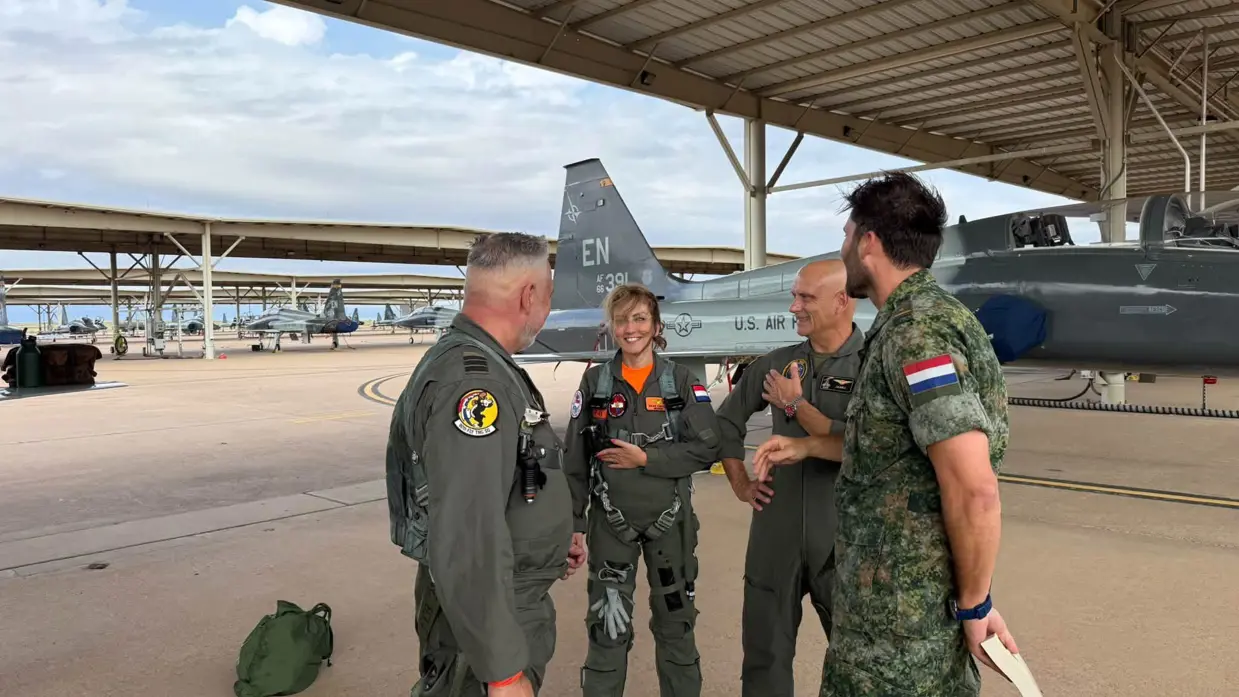 De minister staat op de flightline voor een grijs vliegtuig en is in gesprek met militairen.