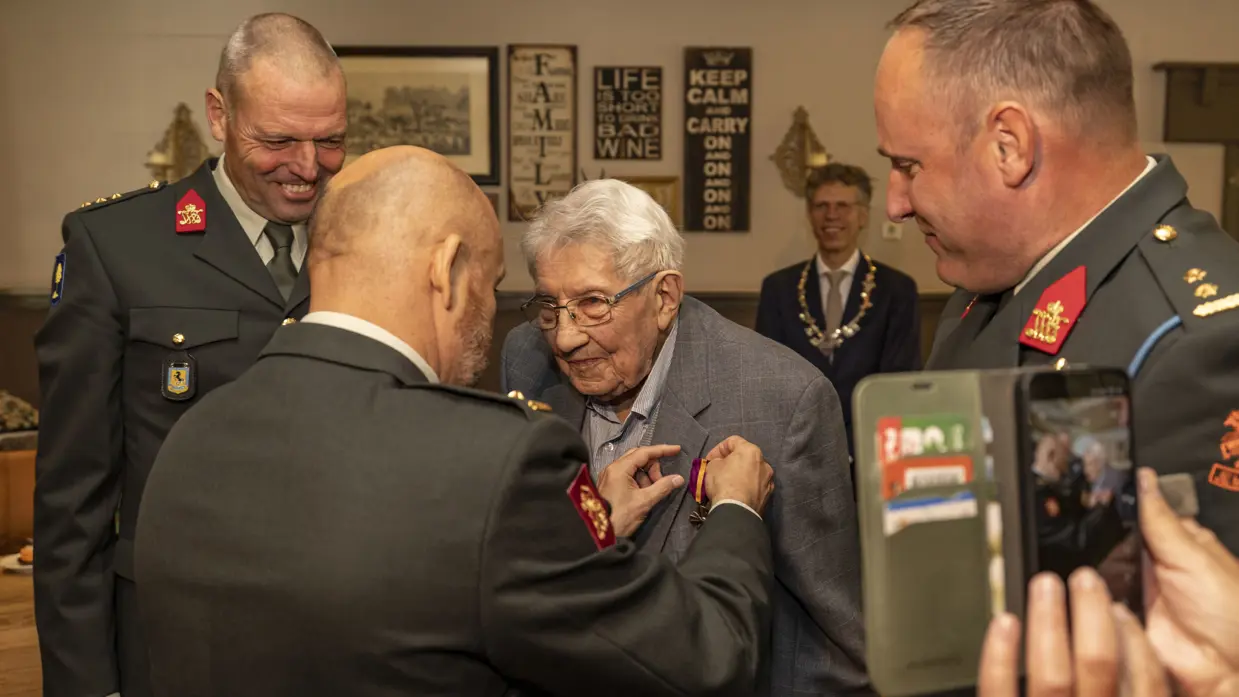 Een bejaarde man krijgt een medaille opgespeld door RMWO majoor Marco Kroon.