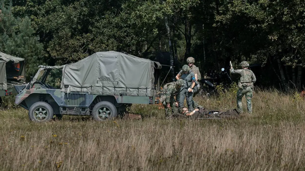 4 militairen met een gewonde op brancard staan achter een Boxer-ambulance.