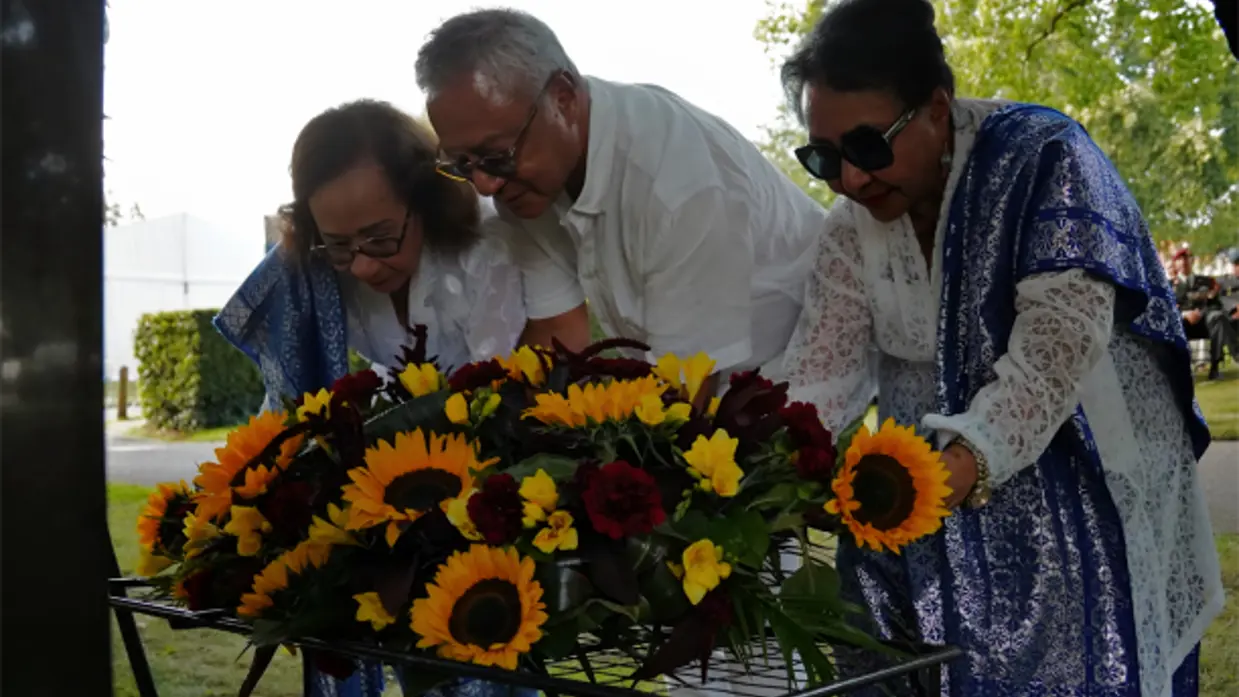 3 mensen leggen een krans met zonnebloemen bij het monument.