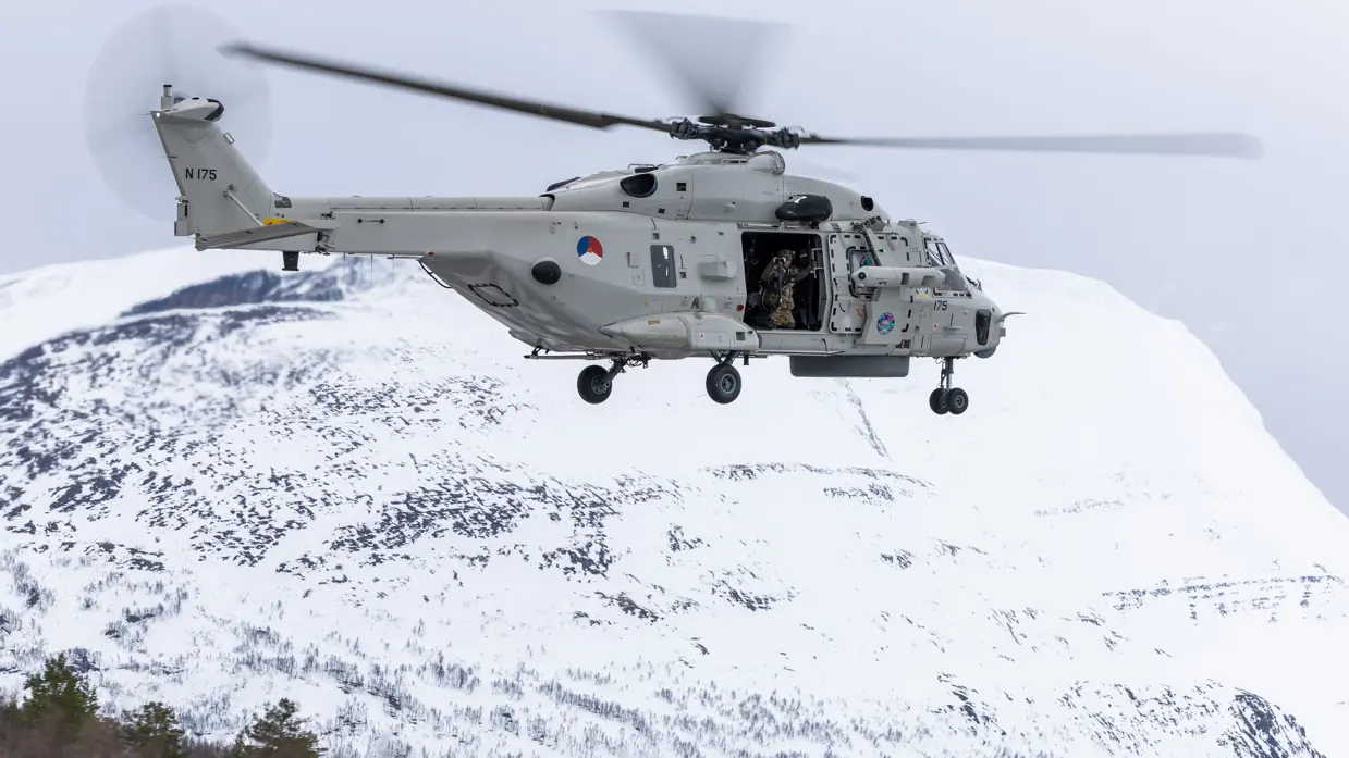 NH90 helikopter in de lucht met op de achtergrond een besneeuwde berg.
