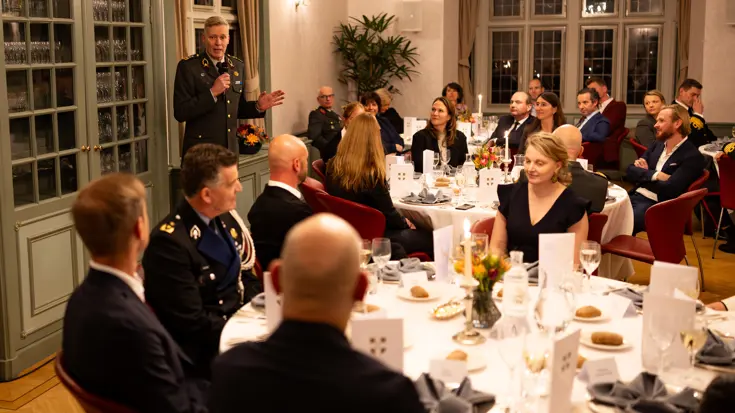 Generaal Maas spreekt de aanwezigen toe in een volle zaal.