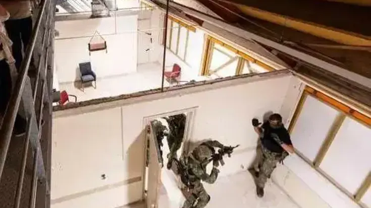 Militairen lopen met wapens in de aanslag door een serie aaneengesloten ruimtes en houden even later een verdachte onder schot.