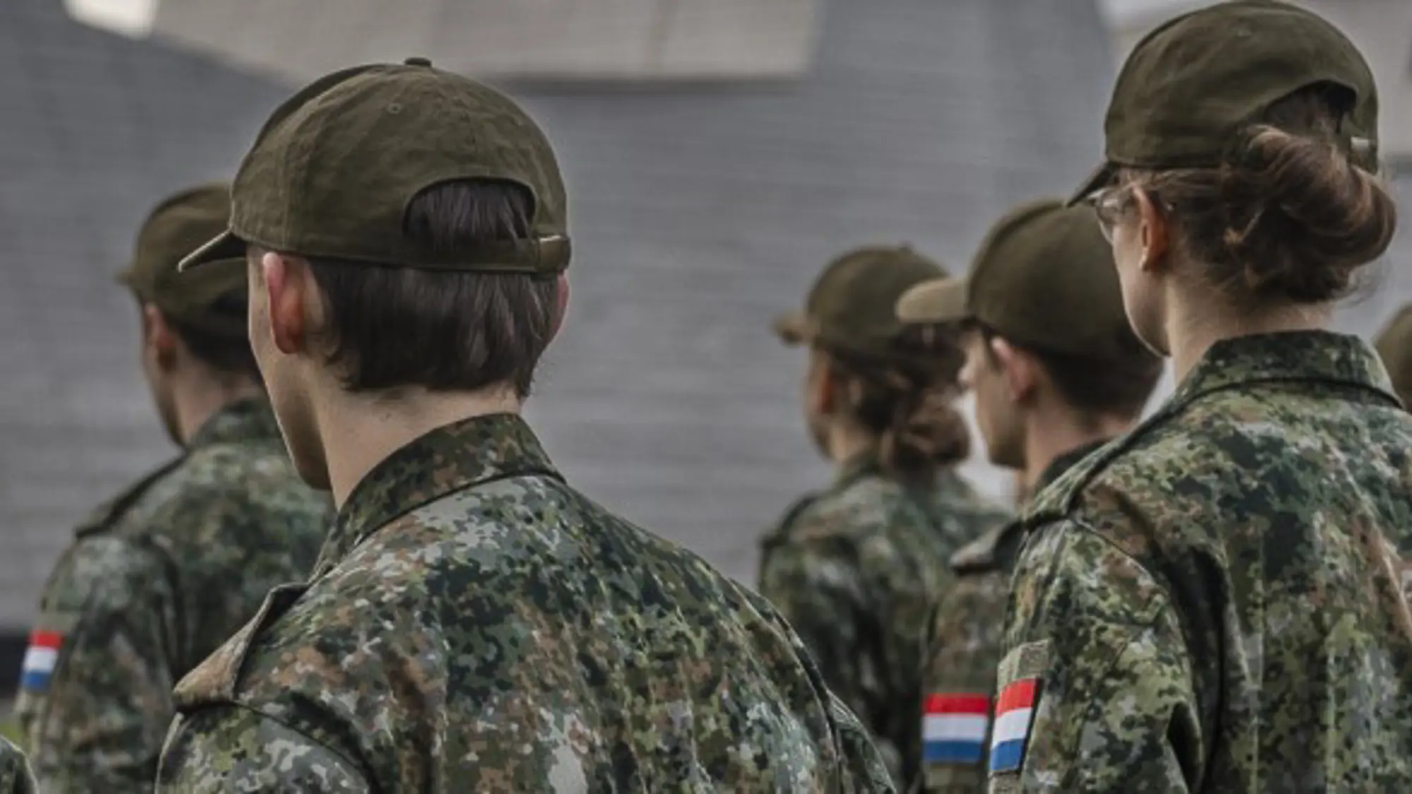 Groep militairen met petjes op de rug gezien terwijl de militairen in rijen staan opgesteld.