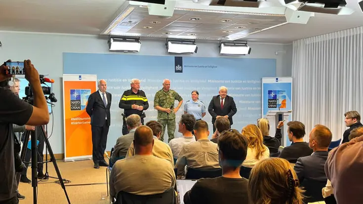 Vijf personen staan voor volle zaal de pers te woord.