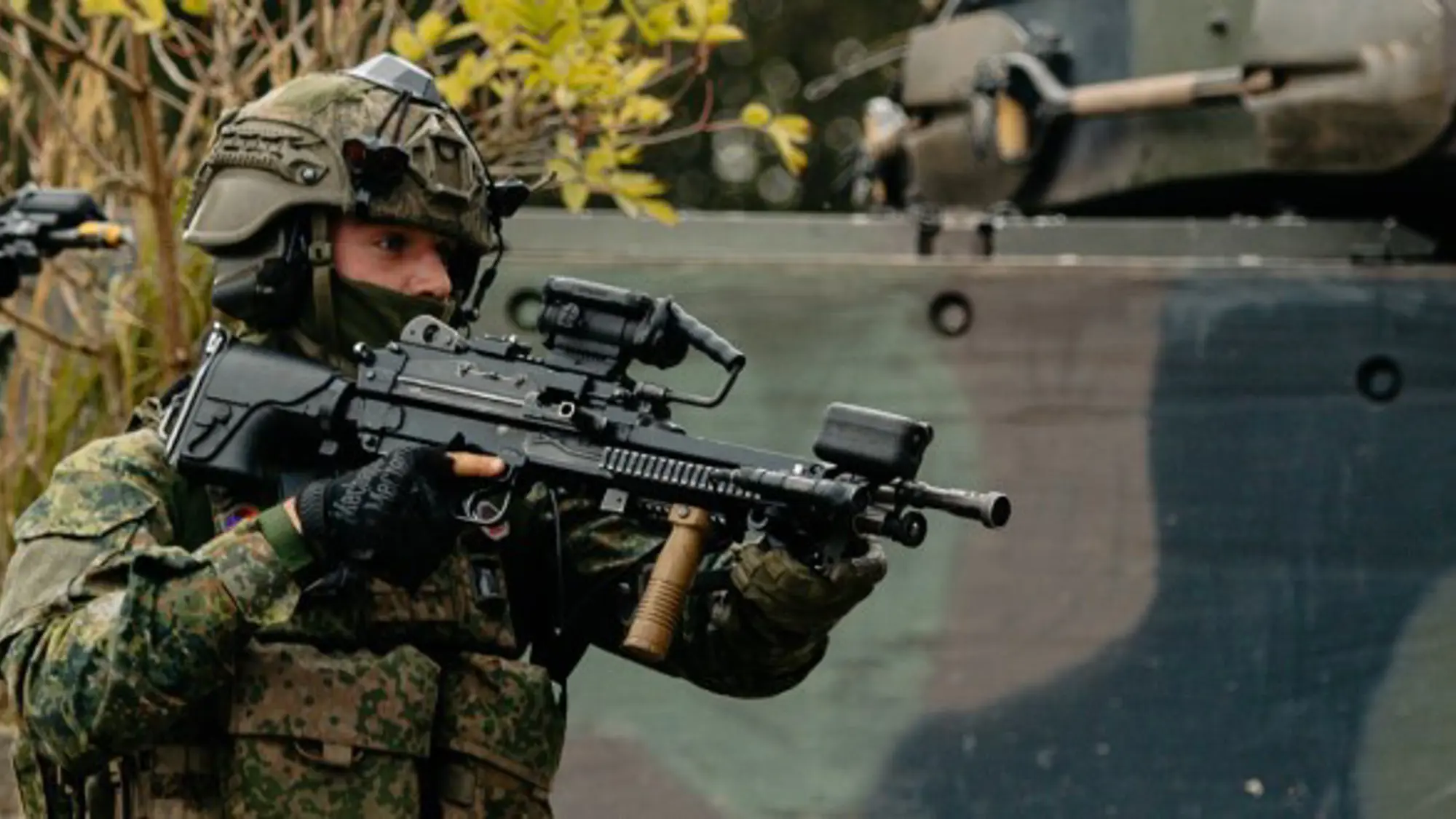 Drie militairen met wapens in de aanslag lopen achter elkaar langs militair voertuig.