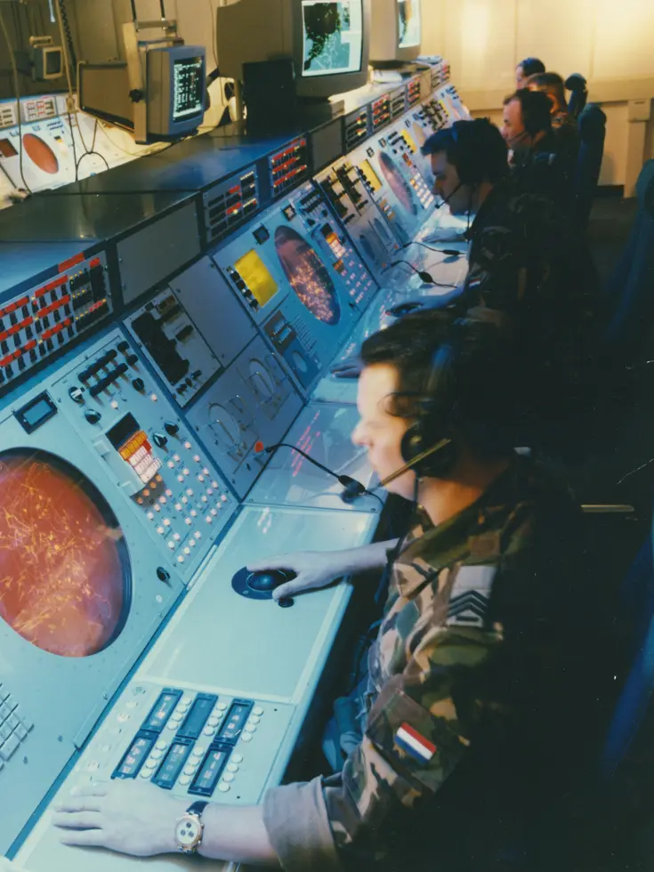 Een aantal militairen in camouflagepak achter oranje radarschermen.