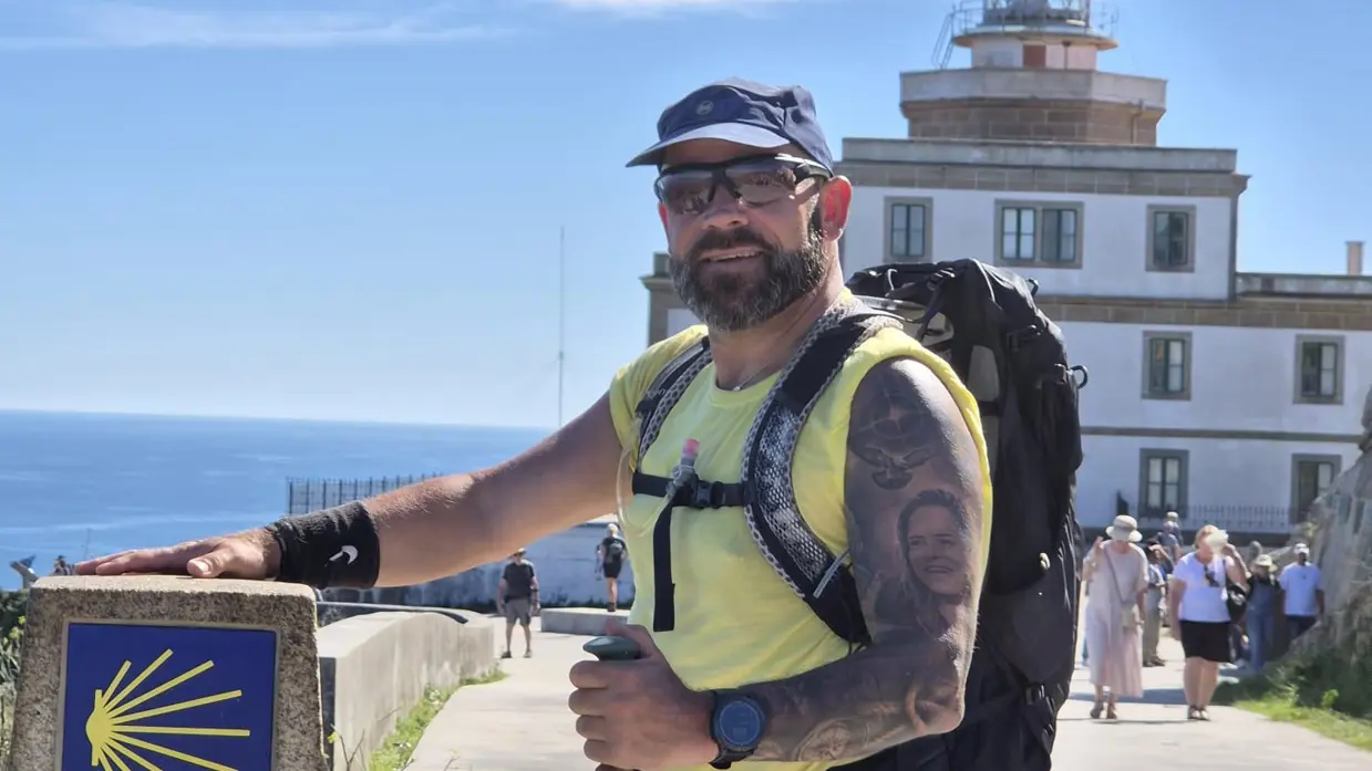  René poseert bij een markering van de route, op zijn arm is een tatoeage van zijn dochter te zien