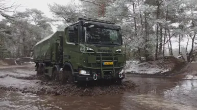 Een truck rijdt door sneeuw en modder, in een grote plas.
