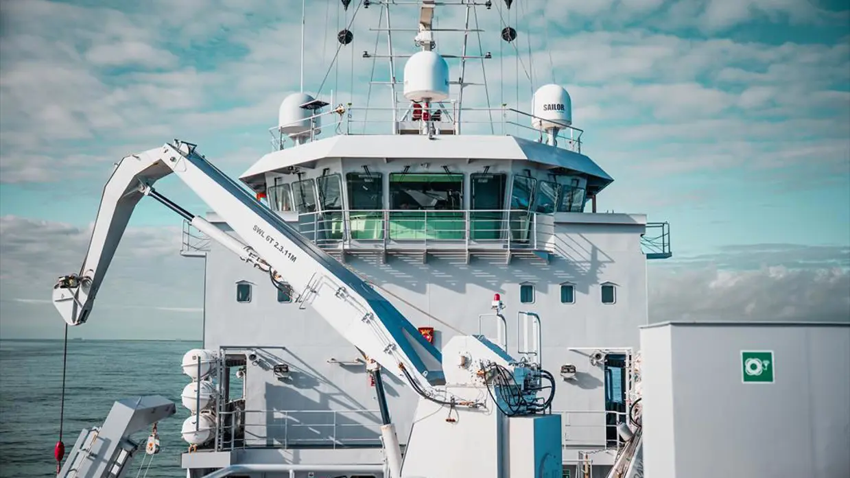 Het voordek van Zr.Ms. Snellius een kraan. En een NH90 voorzien van oefentorpedo in de lucht.