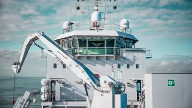 Het voordek van Zr.Ms. Snellius een kraan. En een NH90 voorzien van oefentorpedo in de lucht.