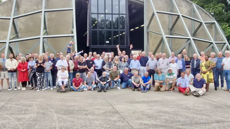 Een groep mensen poseert voor een ronde vliegtuigshelter.