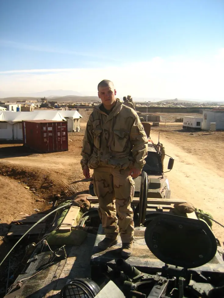 Een jonge soldaat staat in Afghanistan bovenop een pantservoertuig.