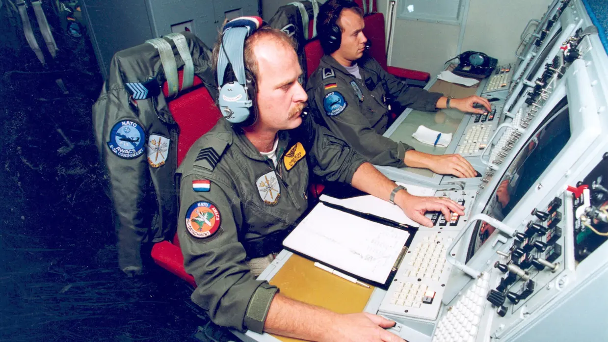 Twee militairen achter radarschermen in een vliegtuig.