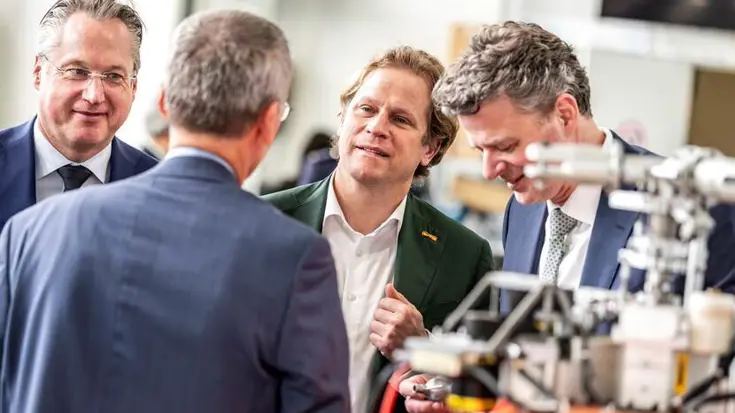 Gijs Tuinman in gesprek met 3 mannen. Op voorgrond niet te identificeren apparaat.