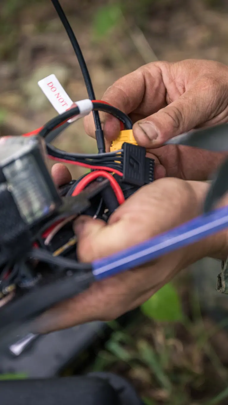 Een drone-operator zit met zijn handen aan een drone. 